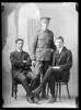 full length portrait of soldier in uniform with 2 other men in suits seated either side