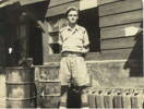 Portrait, standing outside hut with fuel drums and cans lined up beside him - This image may be subject to copyright