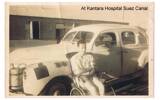 Garden (Gairn) James Robertson (1069) sitting in wheelchair outside, beside a large car, Kantara Hospital, Suez Canal - This image may be subject to copyright