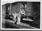 Group, WW2, 2 soldiers standing in front of railway wagons, 3 soldiers inside and another standing on train between wagons. Derek England is in front, holding a pipe. (Collection of Derek Robert England) - This image may be subject to copyright