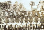 Group photo, WW2, 18 soldiers [?Signals] posed in front of stone front row all wearing shorts, cocnut plams and other palm trees in background. - This image may be subject to copyright