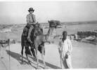 U. Cullen on a camel. The caption on the reverse reads: The Hon. Pte Edna on her Noble Steed. Mean Pyramids. Ruins on Right and Wog Village in background. - This image may be subject to copyright