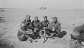 Group photograph of five soldiers and machine gun, taken in the Western Desert November 1941. Preparing to go into action were: Left to right - Laurie Daly, No. 2; Johnnie Black, Range Taker; Bert Hambling, No. 3; Ted O'Connor, No. 4; George Woolf, No. 1; and Pooky Walker, Driver (backside only!). Written on the reverse of the photo: "We all came home. Note the beards, water shortage quite acute, none for shaving etc. only for drinking." - This image may be subject to copyright