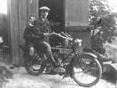 Charles Pratt seated on a motor cycle wearing a cloth hat and with a young male passenger. - No known copyright restrictions