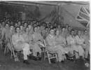 Group of servicemen at an entertainment, seated inside, flag on wall. - This image may be subject to copyright