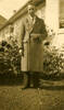 Portrait Leslie Gordon Jackson (66110) standing in civilian clothes, wearing a thick long overcoat in a garden, plants, house windows behind. - This image may be subject to copyright