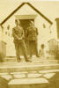 Group, 2 airmen Jesse Pearse and unknown airman smiling standing and a dog sitting on the front steps of a [house?] number 233. - This image may be subject to copyright