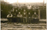 Group, POWs Stalag VIIIB, sitting and standing in front of stacked timber logs Jim Cleaver at front right - This image may be subject to copyright