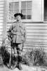 Portrait of Stanley Miller with rifle standing outside in back yard of home - This image may be subject to copyright
