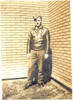 Portrait, 1942, Mills standing, wearing leather jacket, standing in corner of brick walled area. Mills had written the following on the back of the original photograph "25-3-42 - Yours Truly. Taken outside the Dormitory at Dunnville on day of the last flight at Dunnville. I was in a hurry to get back into the air. Hence the clothing and worried expression. Note the flying boots." - This image may be subject to copyright