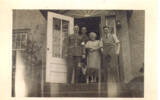 Group, WW2, informal, two airmen in uniform, airman in civilian clothes and woman: From left to right: Lyall King, Jim Shields, Mrs Knoll and Mervyn Jack Mills (NZ414321). Binnie the dog in front, all standing on the steps outside a house. - This image may be subject to copyright