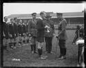 Scales, Thomas Frederick Scales (April 1919). King George V presents the King's Cup to James Ryan, captain of the New Zealand Services Rugby Team, after the team's win in the Inter-Services Tournament at Twickenham rugby ground, London in 1919. Major General Charles William Melvill and another officer look on. The team some of whom have fern leaf emblems on their jerseys are standing in a line. Arthur Percy Singe (third from the left). A film cameraman appears in the background. Royal New Zealand Returned and Services' Association Collection, Alexander Turnbull Library, Wellington, New Zealand (1/2-014258-G). Image has no known copyright restrictions.