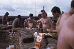 John Nicholl with the cups canteen, Wi Taepa looking down at his kai, behind John, Bill Teller next to him with cup raised PP Brown. Image taken by Lance Corporal Te Hira Wati Heremaia (38481) during active service in the Vietnam War c.1960s. Part of a collection of 150 slides kindly provided by whānau for scanning. © Heremia Whānau (Heremaia-VTM114).